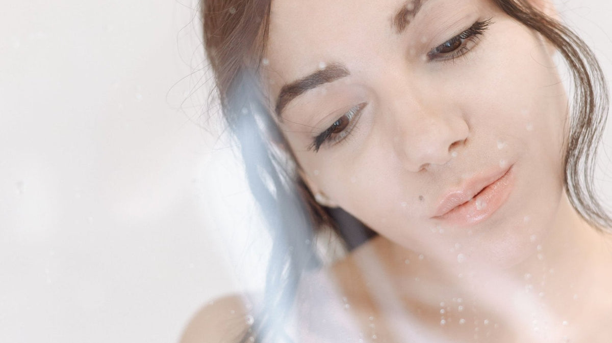 Ragazza dietro un vetro bagnato di gocce, pelle fresca e luminosa