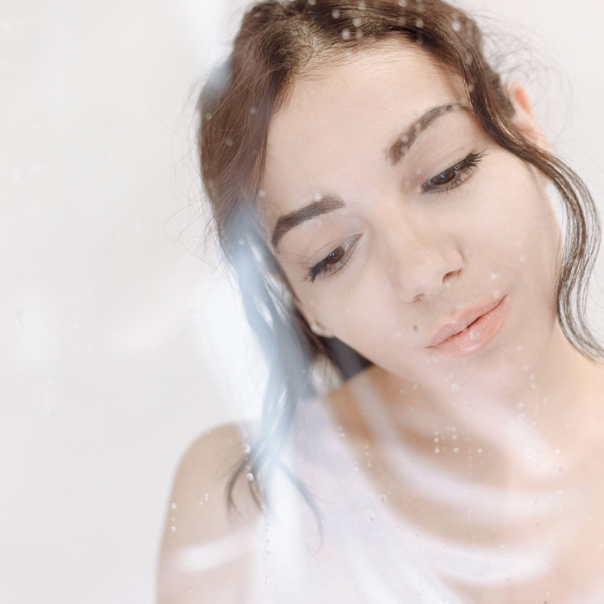 Ragazza dietro un vetro bagnato di gocce, pelle fresca e luminosa